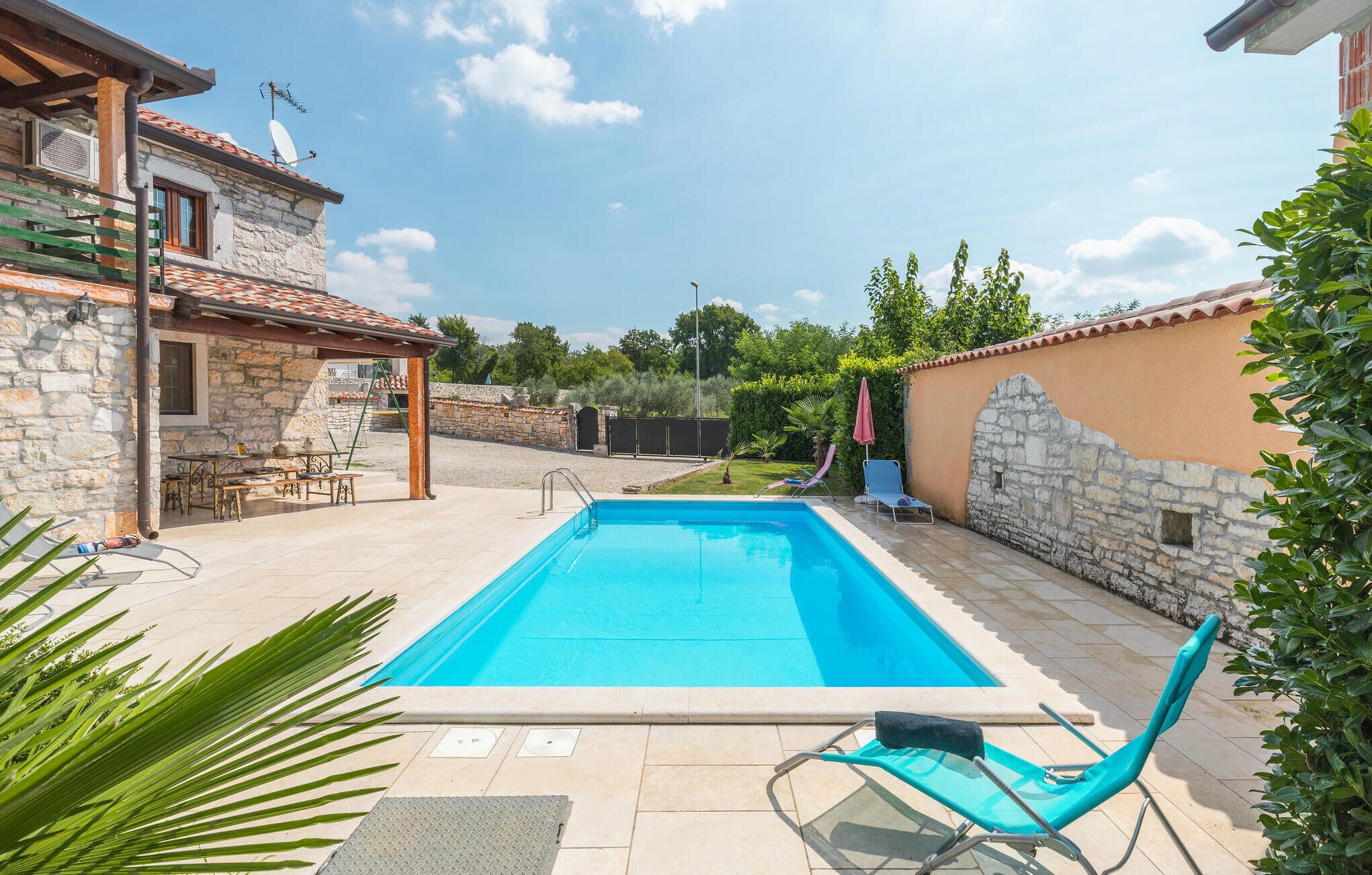 Une piscine avec un mur en pierre et une pergola en bois.