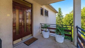 A balcony with a wooden railing, two potted plants, and a door with a textured pattern. - Holiday apartment with balcony and air conditioning (Crikvenica)