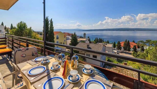 A table set for dining with a view of a body of water and buildings in the background. - Holiday apartment with balcony and air conditioning (Crikvenica)