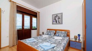 A bedroom with a bed, a nightstand, a wardrobe, and a view through a door. - Holiday apartment with balcony and air conditioning (Crikvenica)