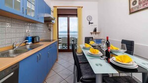 A modern kitchen with blue cabinets, a dining area with a table set for two, and a view through a glass door. - Holiday apartment with balcony and air conditioning (Crikvenica)