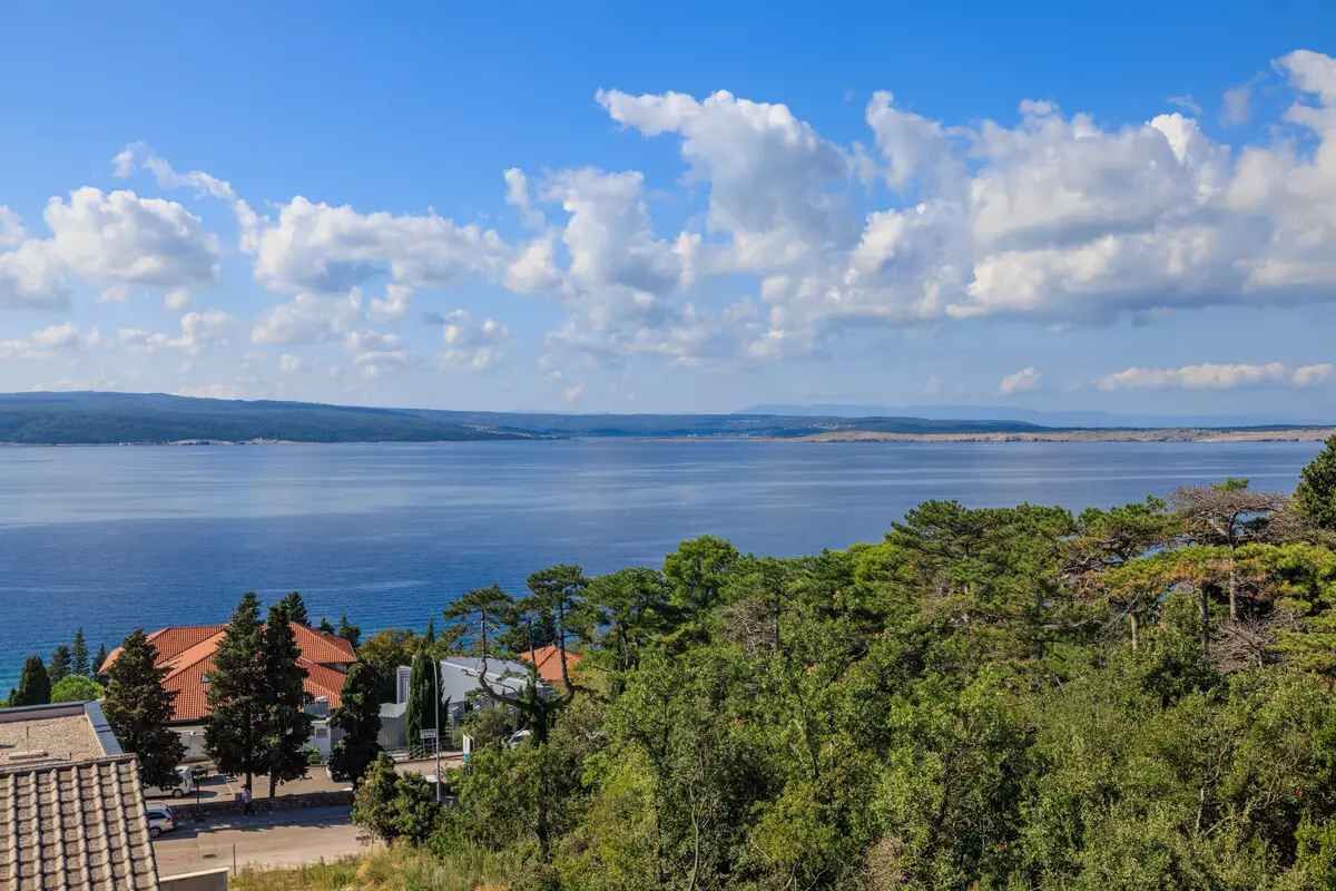 Vista costera con cielo despejado, una masa de agua y una zona residencial con casas y árboles.