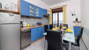 A compact kitchen with blue cabinets, a stainless steel refrigerator, and a dining area with a table set for two. - Holiday apartment with balcony and air conditioning (Crikvenica)