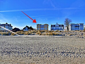A beachfront property with multiple buildings, including a large house with a prominent balcony and a smaller structure.