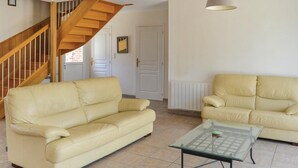 Una sala de estar con un sofá de cuero color beige, una mesa de centro de vidrio, una escalera de madera y una puerta blanca.