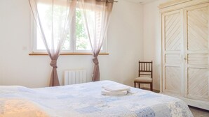 Un dormitorio con una cama, una silla, un armario y una ventana con cortinas.
