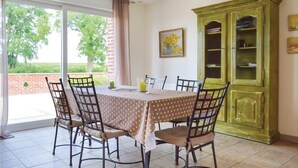 Un comedor con una mesa preparada para cuatro personas, rodeada de sillas, un armario verde y un cuadro en la pared.