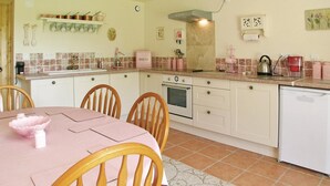 Una cocina con armarios blancos, una mesa rosa y sillas. Hay una estufa, un fregadero y una cafetera.