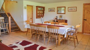 Un comedor con una mesa dispuesta para seis personas, rodeada de sillas de madera. Se observa una escalera a la izquierda que sube a un nivel superior.
