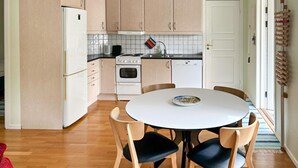 Eine kompakte Küche mit einem runden Esstisch und vier Stühlen, inklusive Kühlschrank, Backofen und Geschirrspüler.