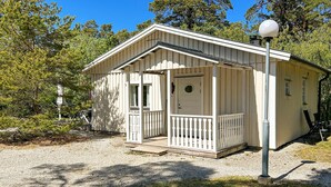 Eine kleine, eingeschossige Holzhütte mit Veranda und Tür, umgeben von Bäumen.