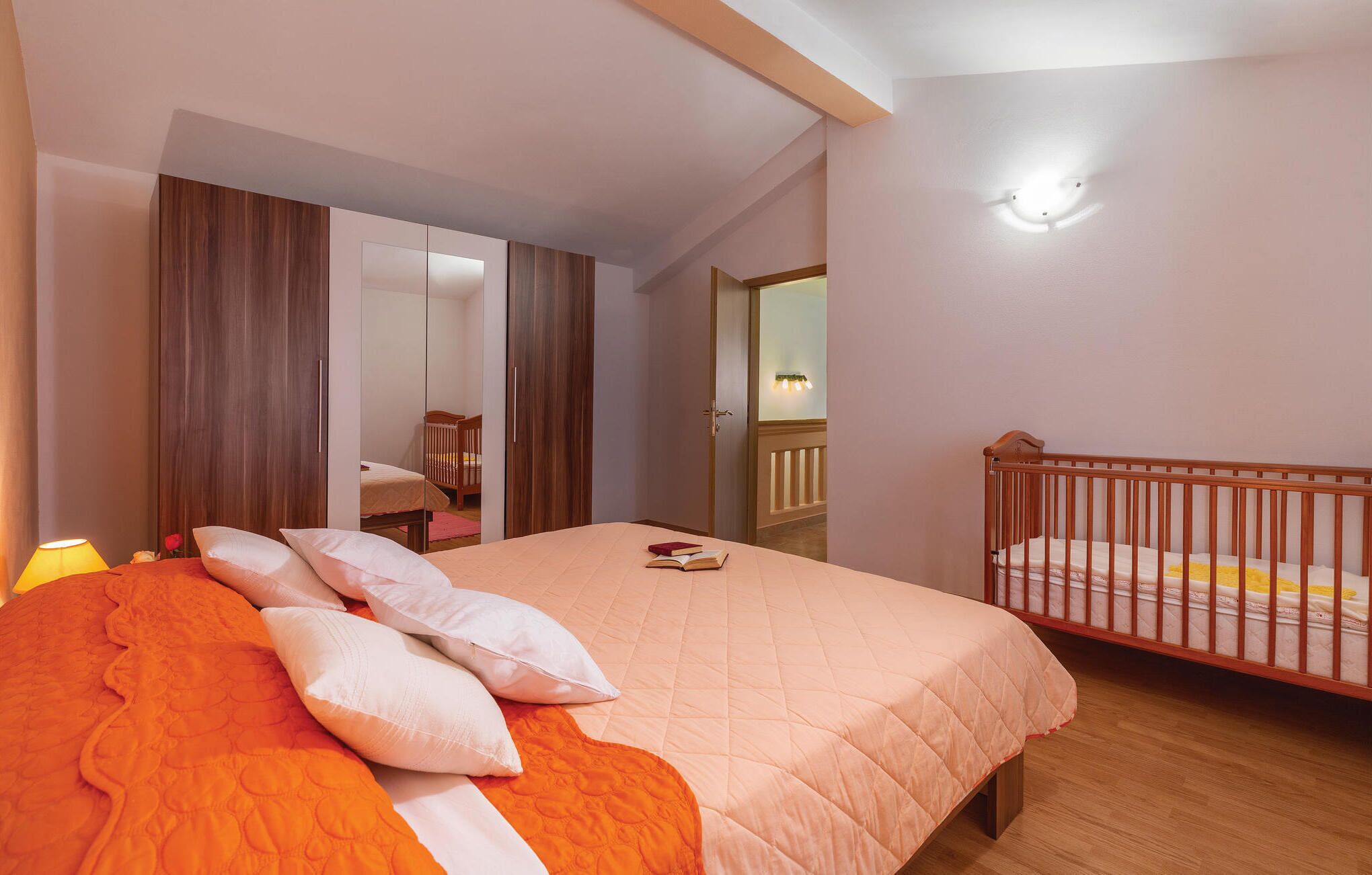 A bedroom with a bed, a crib, a wardrobe, and a mirror.