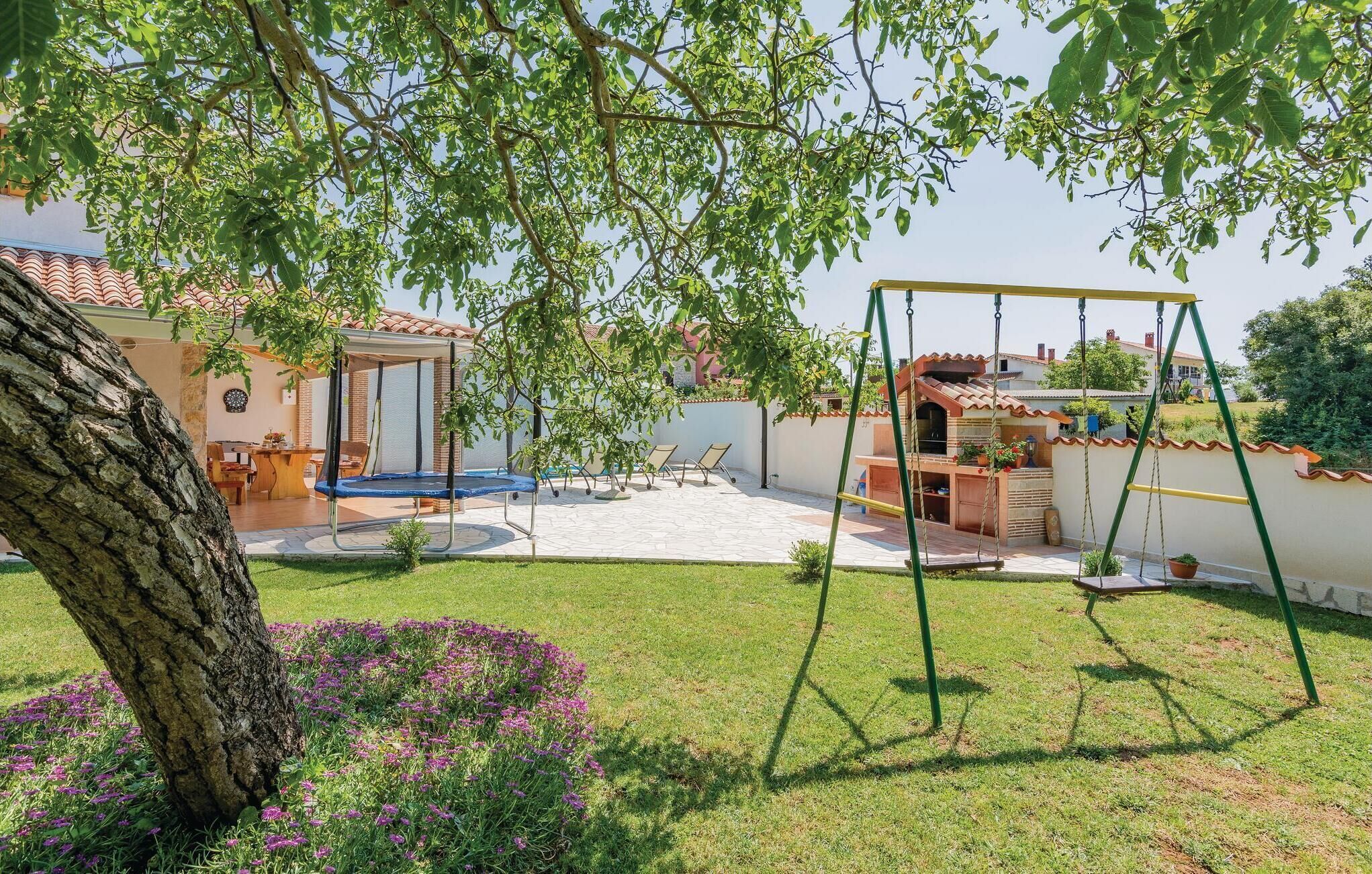 Ein Garten mit Schaukel, überdachter Sitzgelegenheit und einem kleinen Blumenbeet mit violetten Blumen.