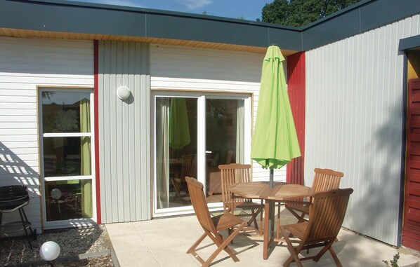 Une terrasse avec une table et des chaises, un parasol vert et une porte-fenêtre coulissante.