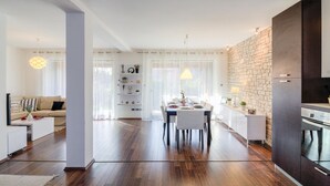 A modern kitchen with a stone backsplash, wooden flooring, and a dining area with a white table and chairs. - Beautiful home in Banjole (Banjole)