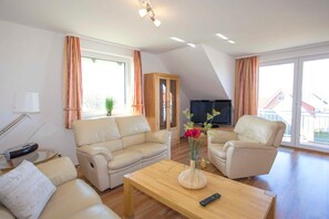 A living room with two sofas, a coffee table, a TV, and large windows with curtains. - BB 3-room apartment 9 - Villa Boddenblick (Wiek)