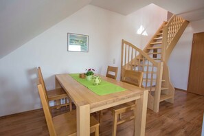 A dining area with a wooden table, chairs, a green placemat, and a wooden staircase. - BB 3-room apartment 9 - Villa Boddenblick (Wiek)