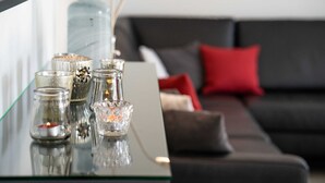 Una mesa de vidrio con velas y elementos decorativos en una sala de estar moderna con un sofá gris y cojines rojos.