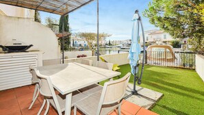 An outdoor patio with a table and chairs, a grill, and a view of a canal with boats. - Beautiful home in Aigues-Mortes with WiFi (Aigues-Mortes)