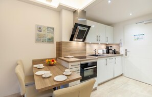 A modern kitchen with white cabinets, a wooden countertop, a built-in oven, and a sink. There is a dining table with chairs and a fruit bowl. - Awesome apartment in Binz with outdoor swimming pool (Prora/Rügen)