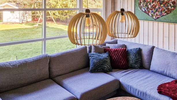 Un salon moderne avec un canapé d’angle gris, deux suspensions lumineuses en bois et une table basse ronde en bois.