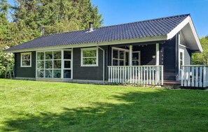 Ein eingeschossiges Haus mit dunkler Fassade, einer Veranda und einem weißen Zaun.