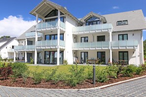 A modern multi-story building with balconies, a covered outdoor area, and a landscaped garden.