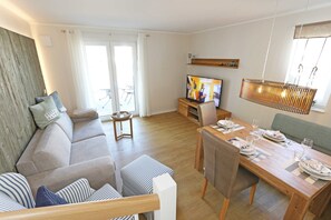 A modern living room with a sofa, a dining table set for two, and a television on a wooden stand.