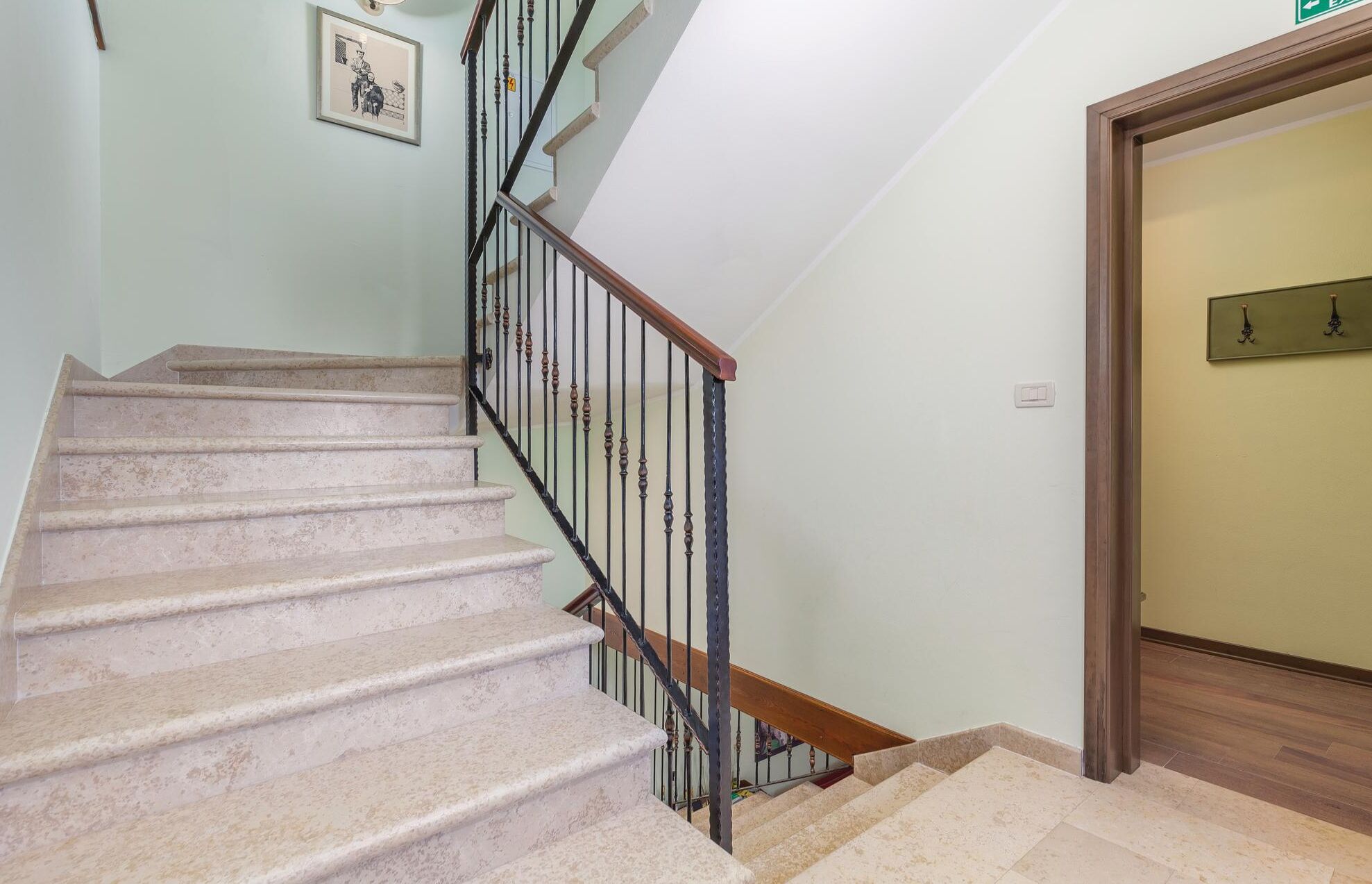 Un escalier avec une rampe en bois et des balustres en métal, menant à une porte sur laquelle est apposée une enseigne.