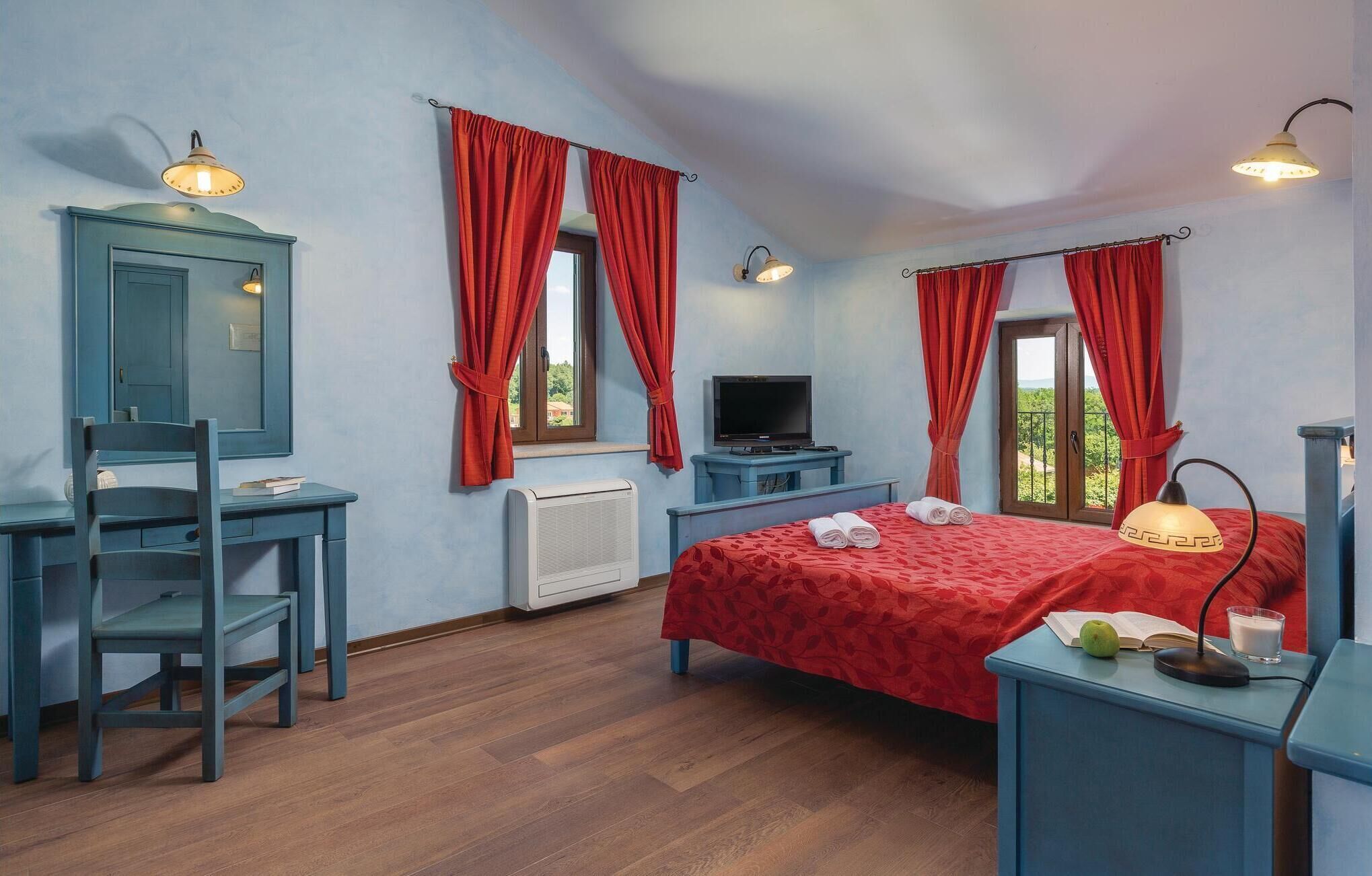 A bedroom with a bed, a desk, a chair, a television, and a window with curtains.