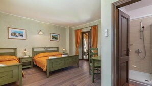 Een hotelkamer met twee bedden, een houten vloer, een badkamer met douche, en twee ingelijste foto's aan de muur.