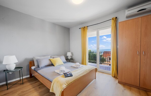 Une chambre à coucher avec un lit, des tables de chevet, une armoire et un balcon agrémenté de rideaux jaunes.