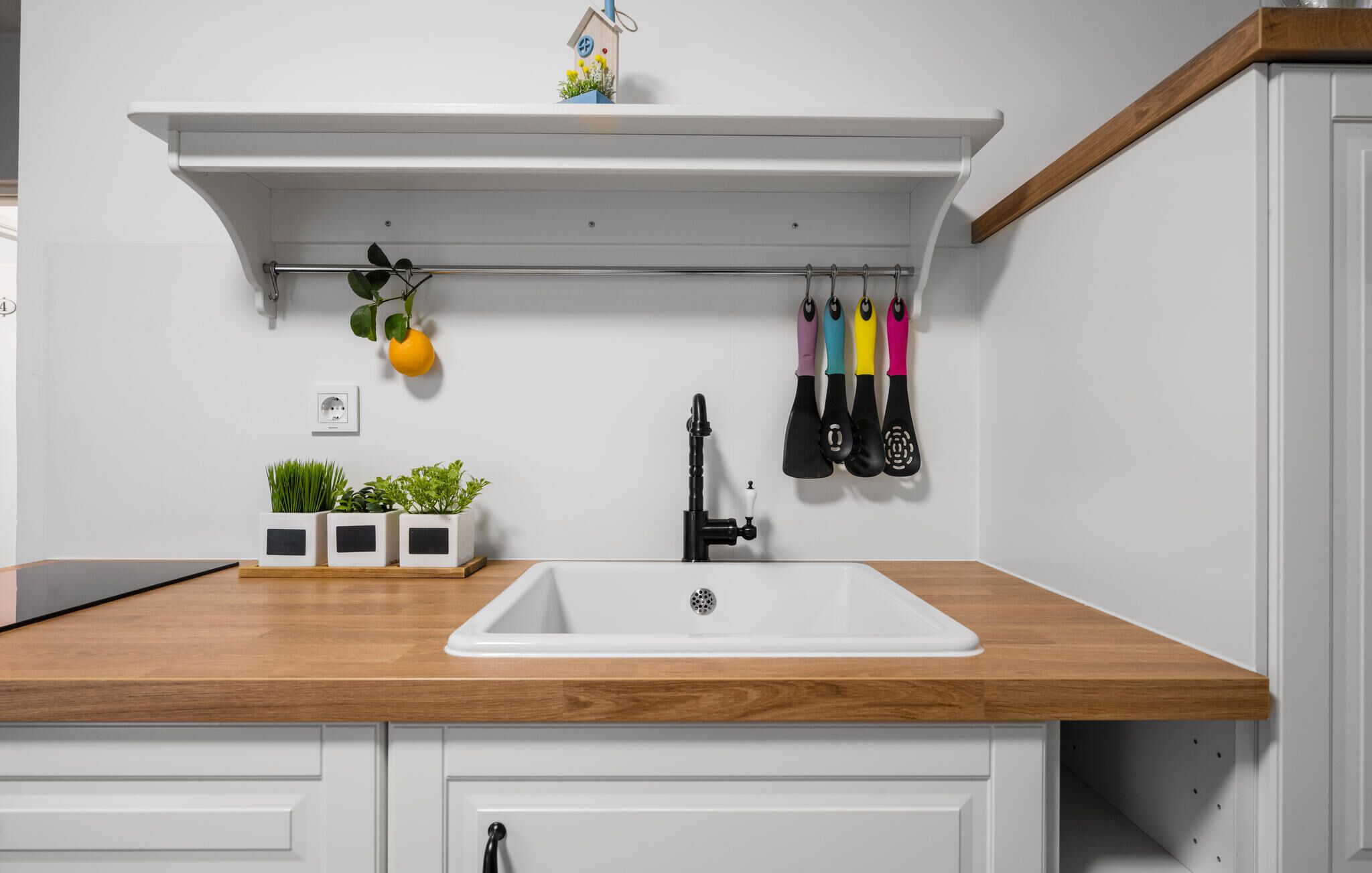 A kitchen with a wooden countertop, a white sink, and a hanging rack with kitchen utensils.