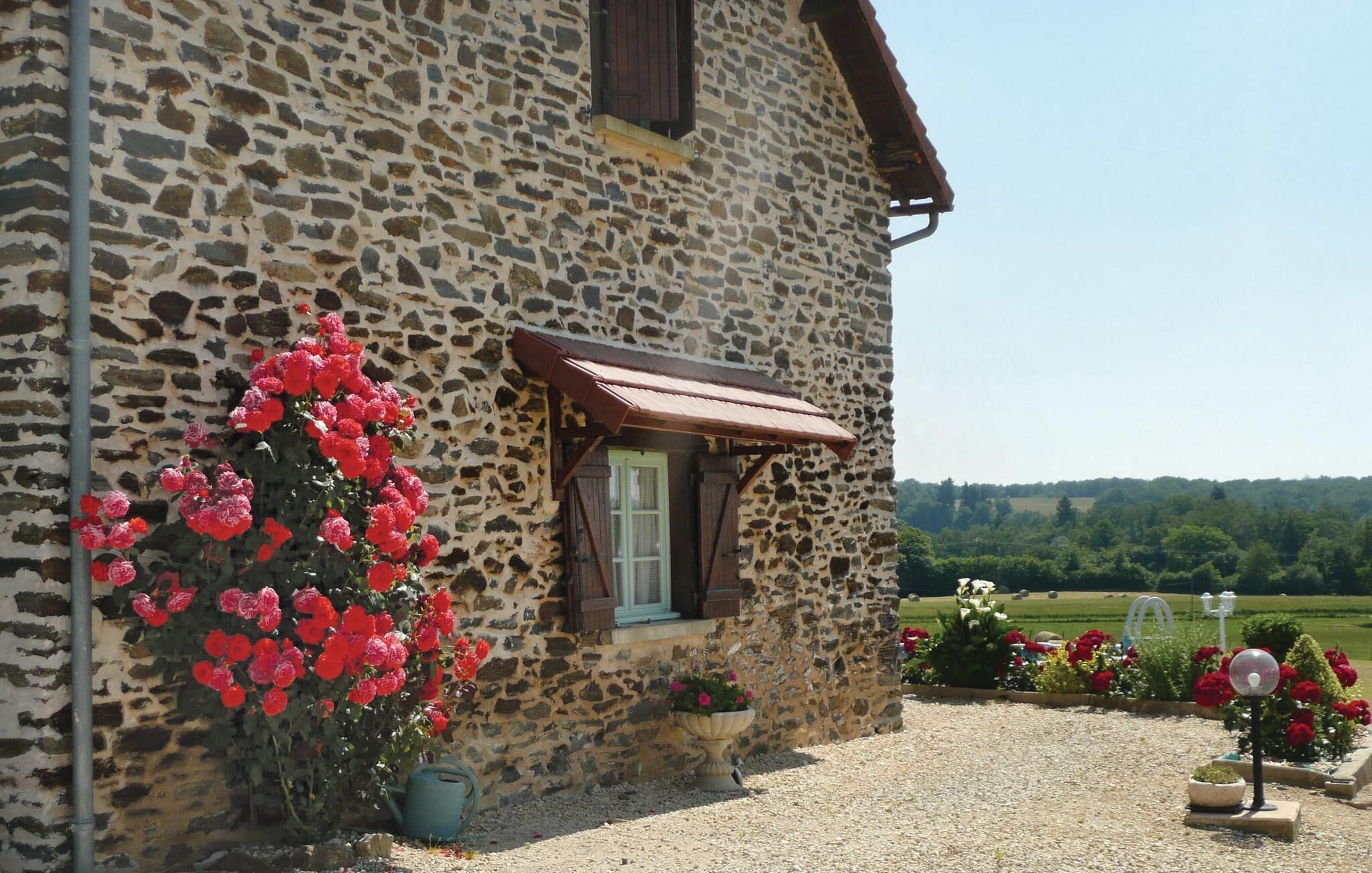 A stone building with a window and a door, surrounded by gravel and flowers.