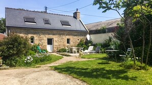 Een stenen huis met een grindpad, een tuin met groene planten en tuinmeubilair.