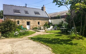 Ein Steinhaus mit Kiesauffahrt, ein Garten mit grünen Pflanzen und Gartenmöbeln.
