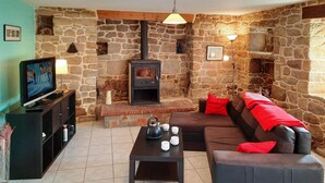 Ein gemütliches Wohnzimmer mit Steinwand, Kamin, einer Couch mit roten Kissen, einem Fernseher und einem Couchtisch.