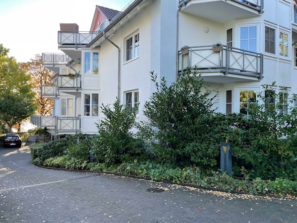 A multi-story residential building with balconies, a paved driveway, and surrounding greenery.