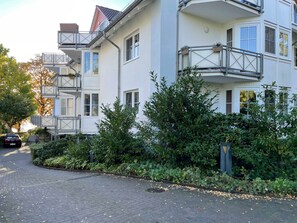 Ein mehrgeschossiges Wohngebäude mit Balkonen, einer gepflasterten Auffahrt und umgebender Bepflanzung.
