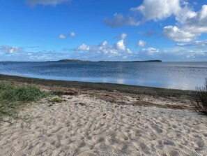 Una spiaggia sabbiosa con un mare calmo e isole in lontananza, sotto un cielo parzialmente nuvoloso.