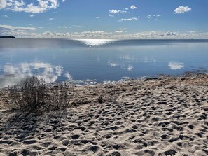 A beach with clear water reflecting the sky and clouds.