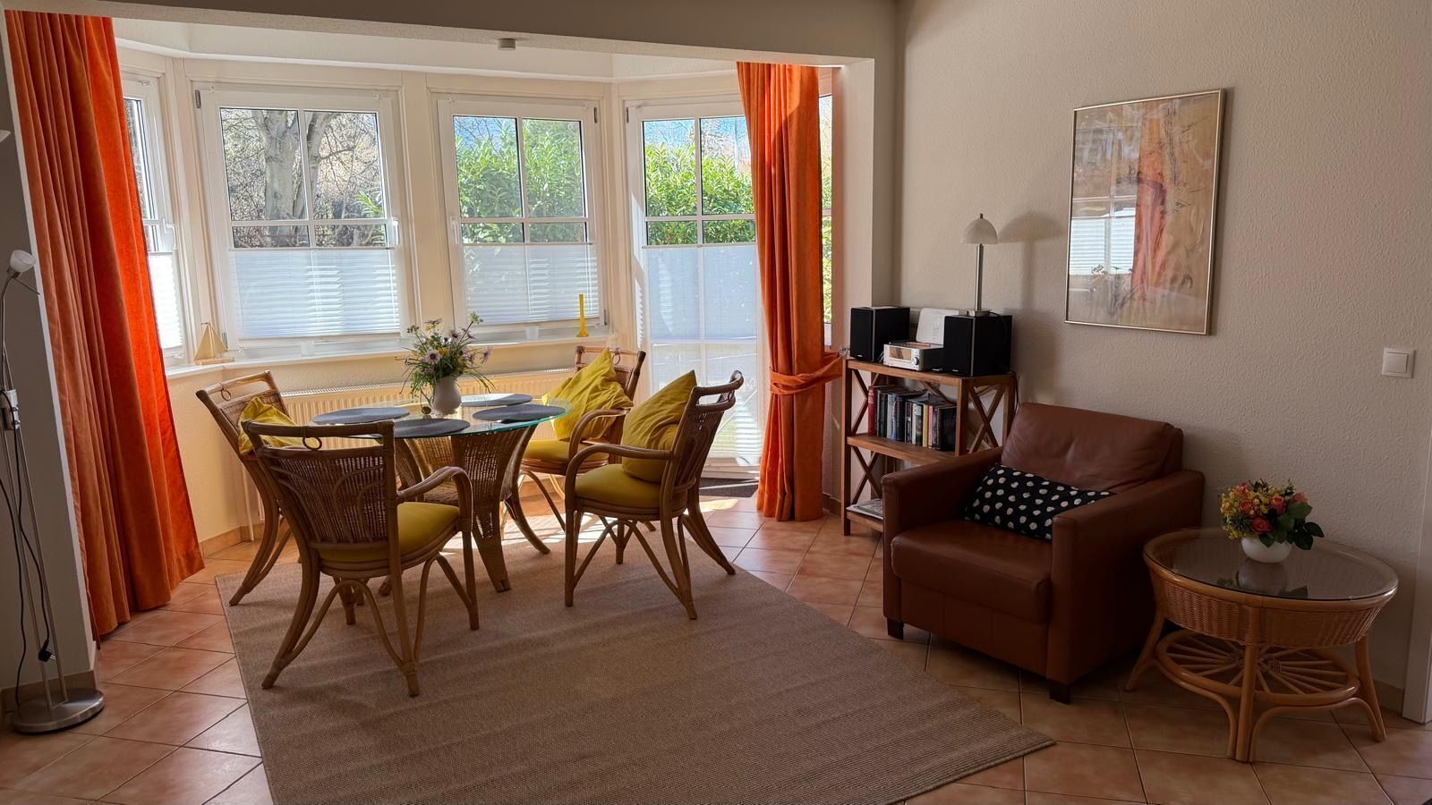 Ein Wohnzimmer mit Essbereich, einer Couch, einem kleinen Tisch mit einer Vase und einem Bücherregal.