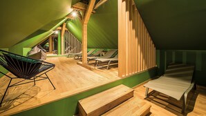Um quarto com teto inclinado, vigas de madeira, uma cama, uma cadeira e uma mesa.