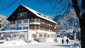 A traditional wooden building with multiple windows and balconies, a sign indicating it's a hotel, and a snowy landscape with mountains in the background.
