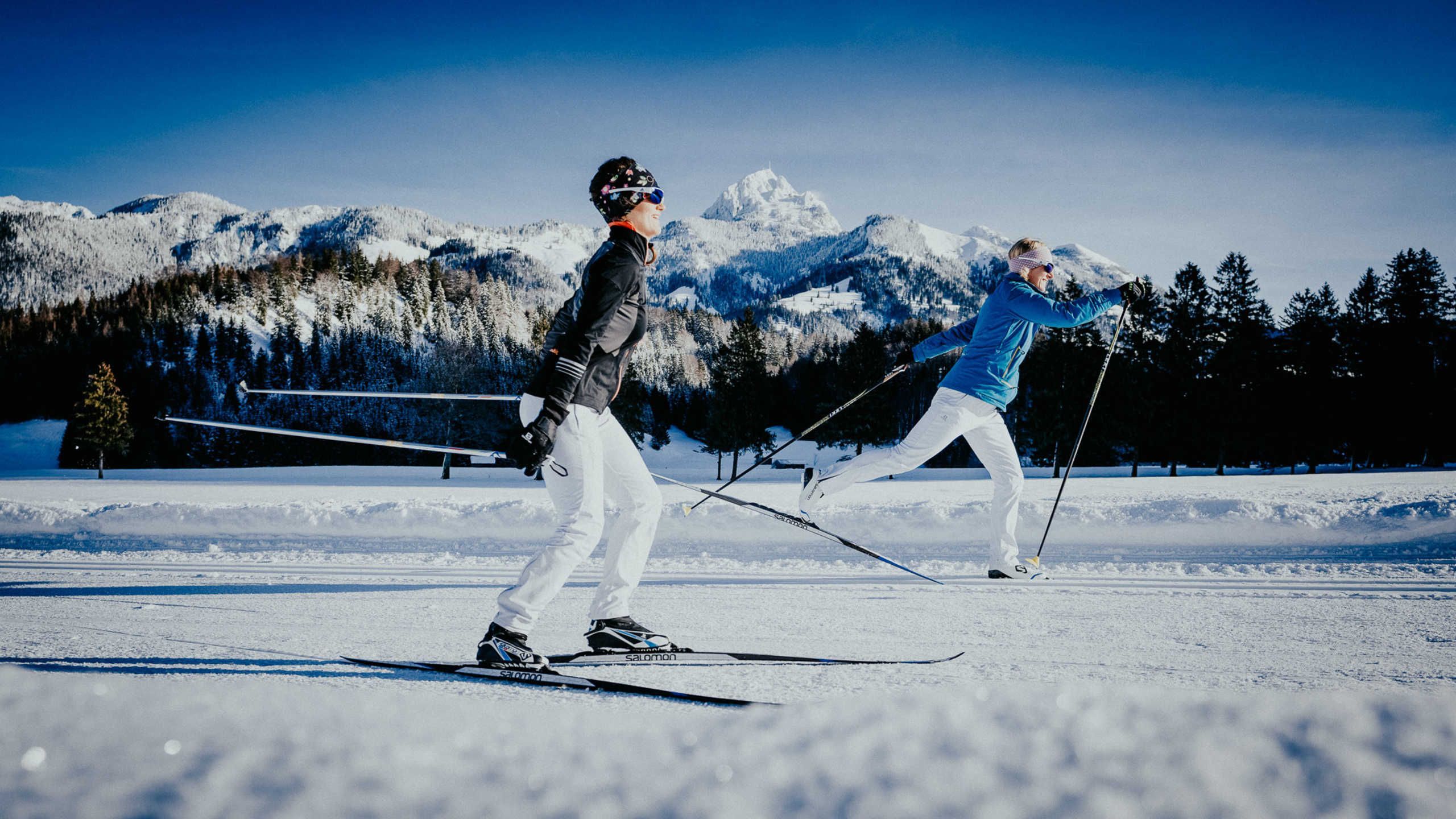 Twee skiërs op een besneeuwde helling, met bergen op de achtergrond.