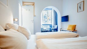 Quarto de hotel com duas camas, televisão, janela com cortinas, mesa pequena e uma cadeira.
