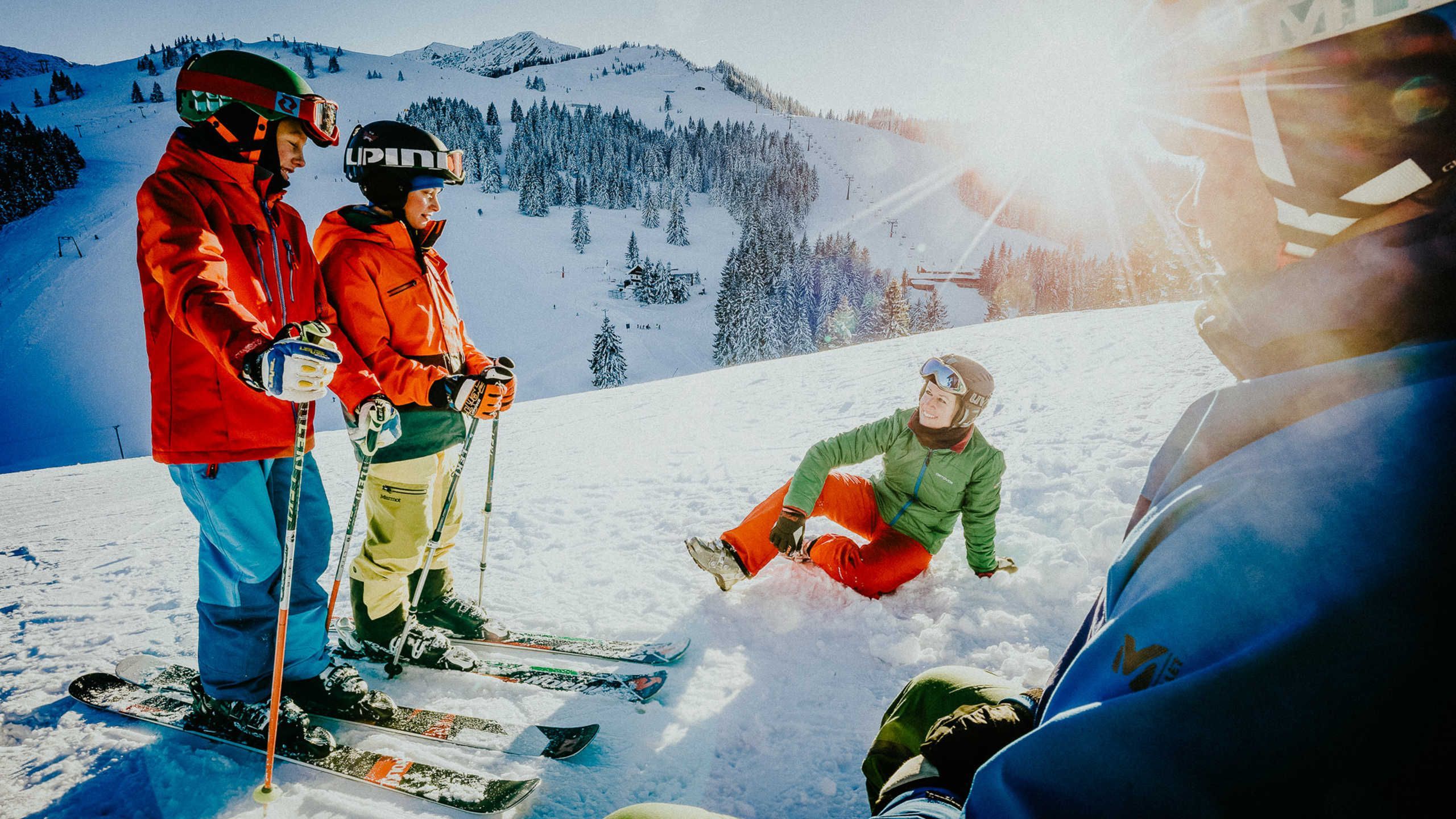 A group of people on a snowy slope with ski equipment, a clear sky, and a mountain in the background.