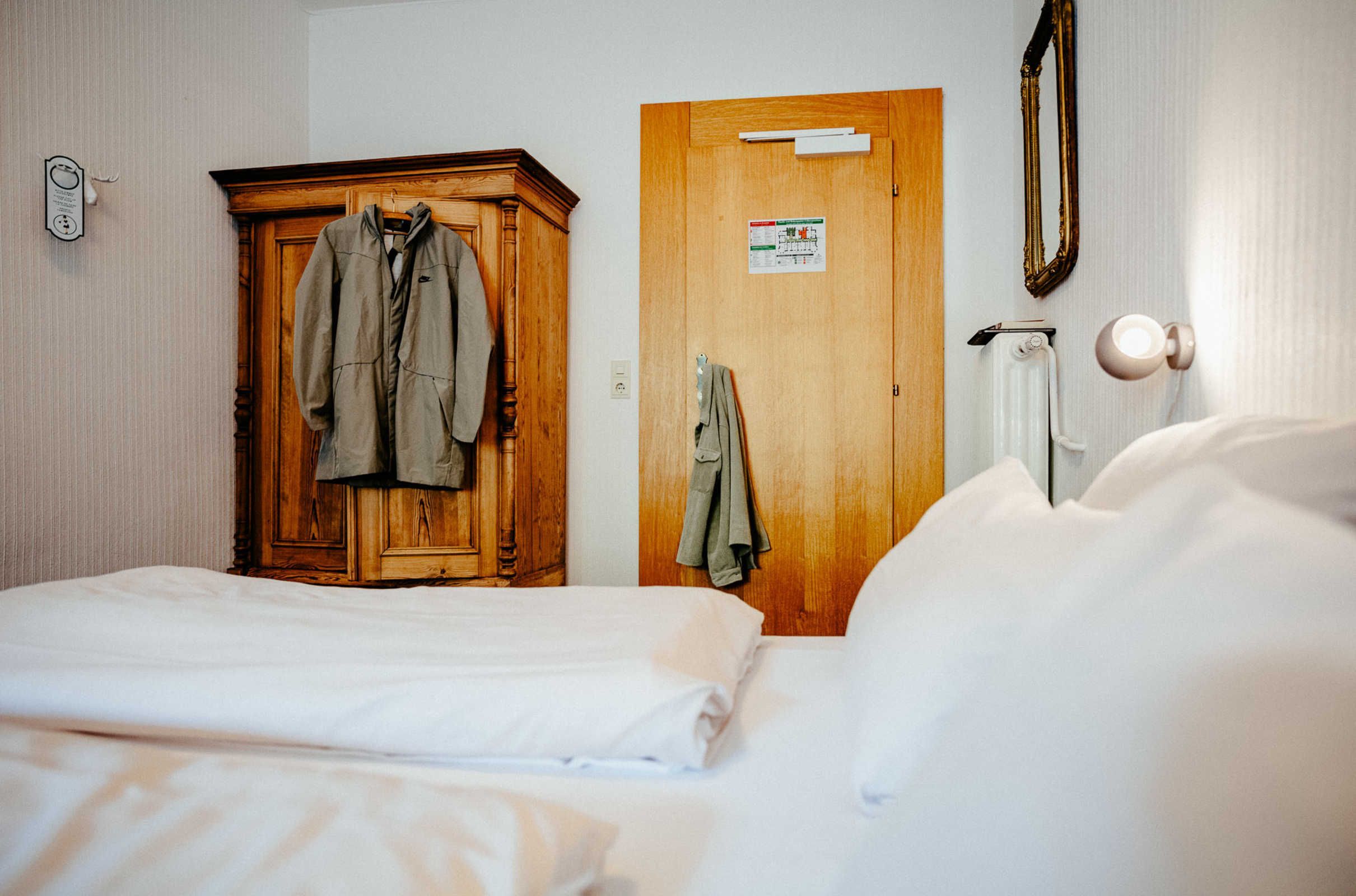 Ein Hotelzimmer mit einem Bett, einem Holzschrank, einer Tür mit einem Schild und einem Spiegel an der Wand.