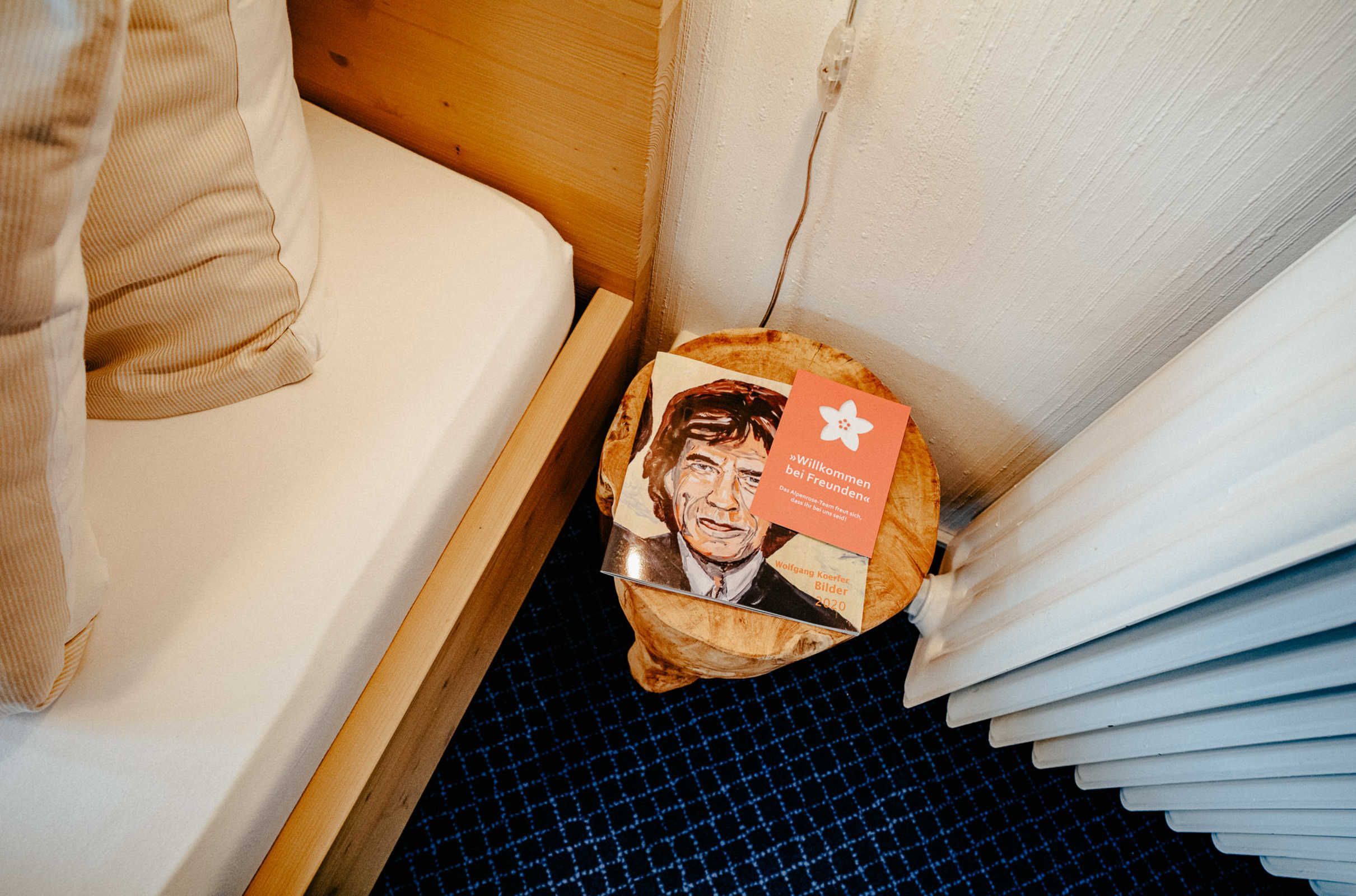 Een bed met een houten hoofdbord, een klein houten nachtkastje en een blauw geruit vloerkleed.