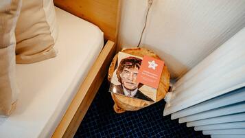 Een bed met een houten hoofdbord, een klein houten nachtkastje en een blauw geruit vloerkleed.